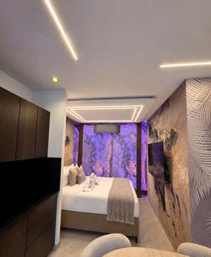 Une chambre moderne avec un lit, un téléviseur à écran plat, une armoire en bois et un mur décoré d’œuvres d’art abstraites.