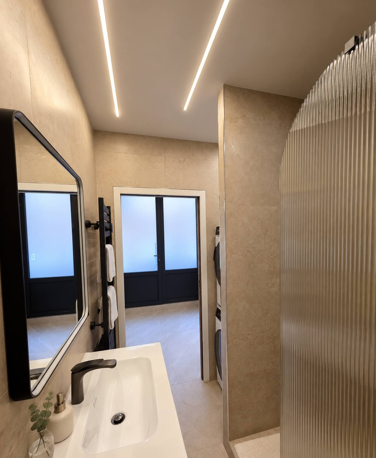 Une salle de bain moderne avec un grand miroir, un lavabo blanc et un espace douche.