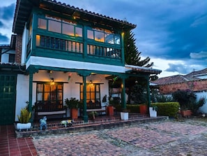 A two-story building with a balcony, a covered porch, and potted plants. - Hotel Altair (Villa de Leyva)