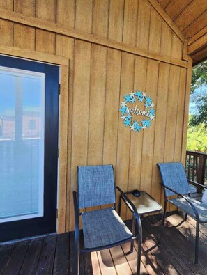 A wooden deck with two chairs and a small table, a 'Welcome' sign, and a window with blinds. - Exotic Shores at Lake Conroe (Willis)