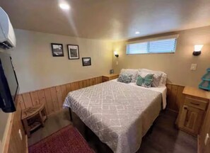 Ein Schlafzimmer mit einem Bett, einem Holzkopfende, einer Wandleuchte und einem kleinen Hocker.