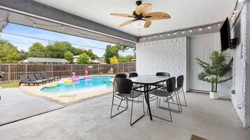 En udendørs terrasse med pool, ventilator i loftet og et spisebord med stole.
