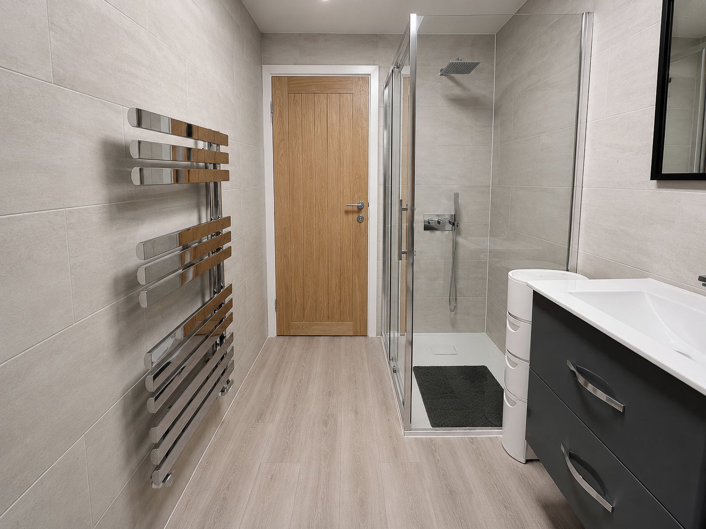A modern bathroom with a shower, a glass-enclosed shower area, a wooden door, and a white sink with a dark cabinet.