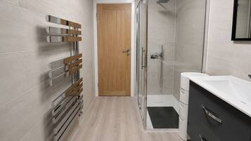 A modern bathroom with a shower, a glass-enclosed shower area, a wooden door, and a white sink with a dark cabinet.