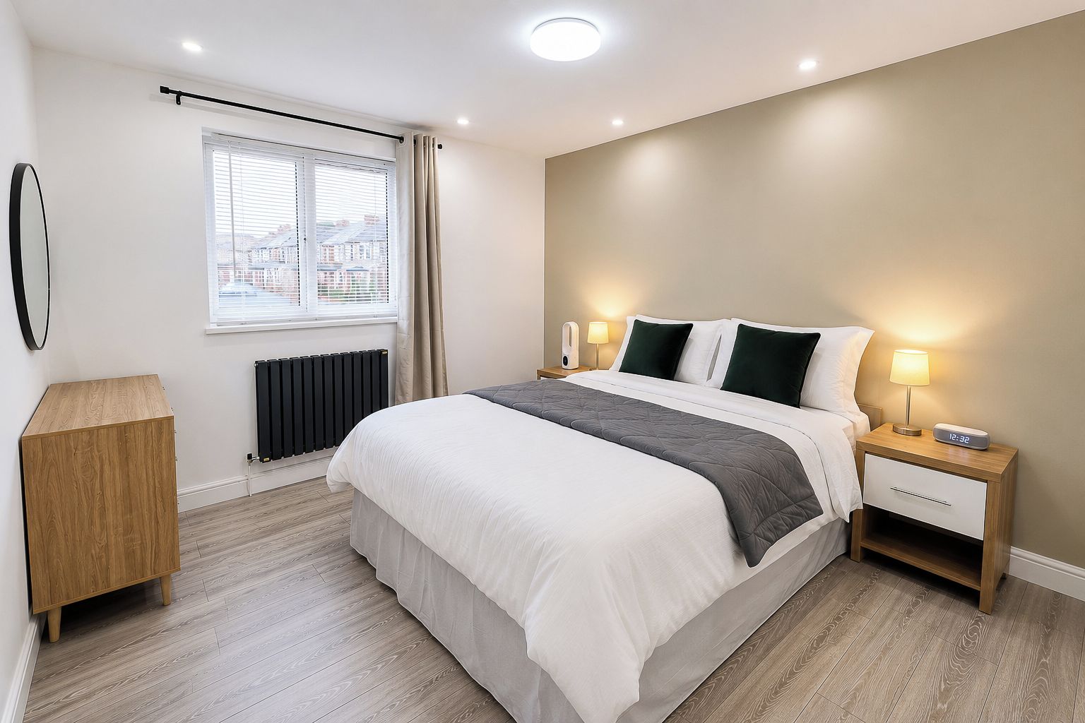 A modern bedroom with a bed, bedside lamps, a nightstand, a radiator, a window with blinds, and a wooden cabinet.