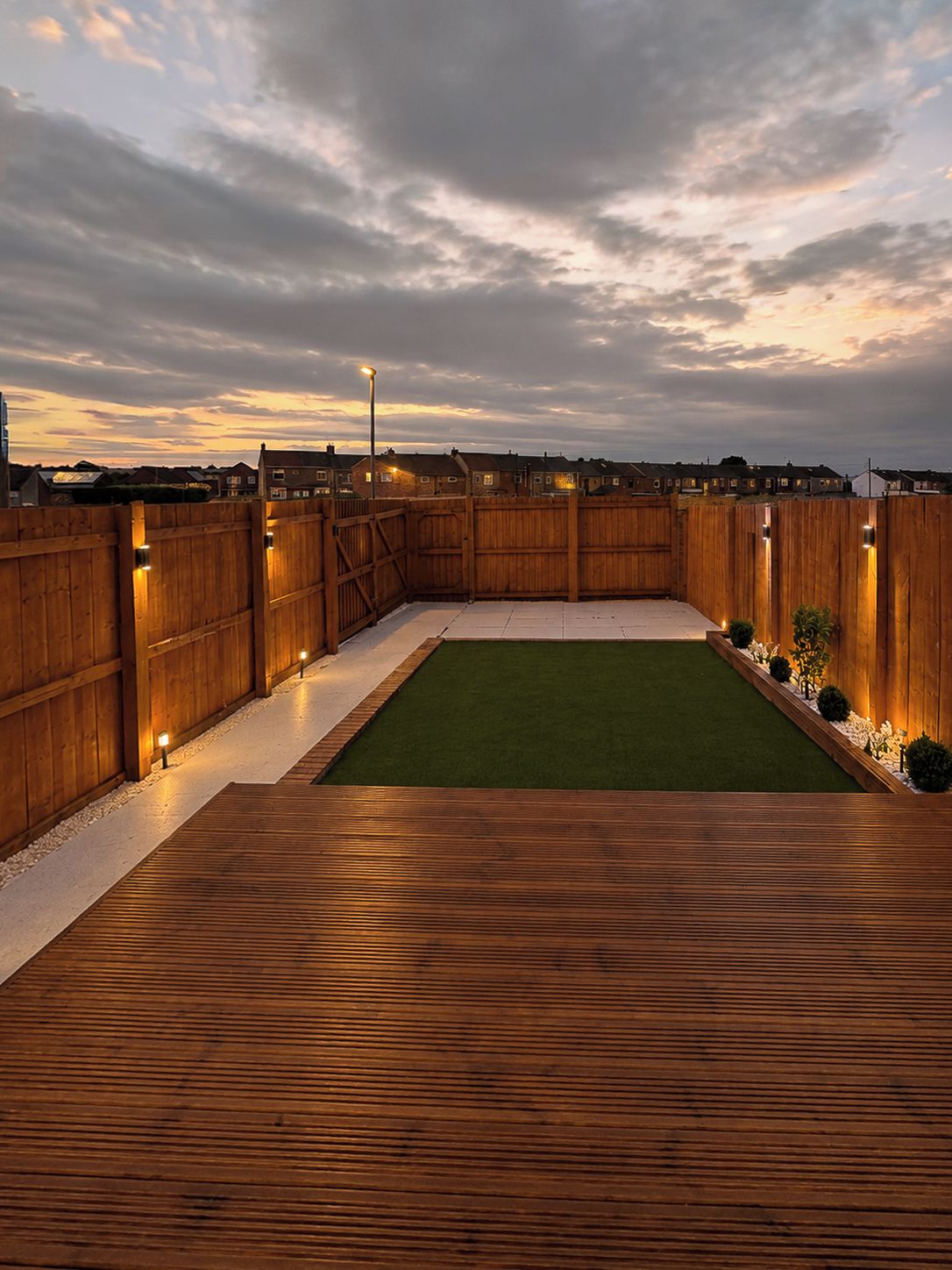 A wooden deck with a green artificial turf area, surrounded by a wooden fence with lights.