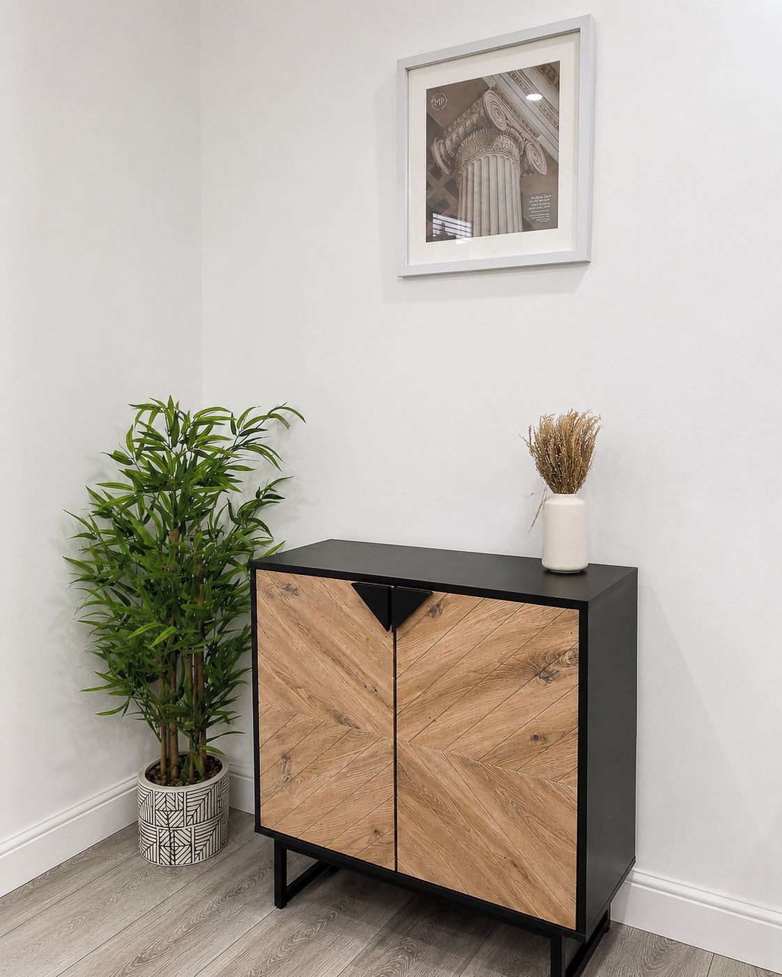 Ein Eckzimmer mit einem schwarzen Holzschrank, einer Topfpflanze und einem gerahmten Bild an der Wand.
