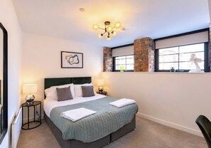 A hotel room with a bed, bedside lamps, a wall-mounted picture, a window with a view, and a modern chandelier. - Luxury City Centre Apartment with Canal View (West Midlands)