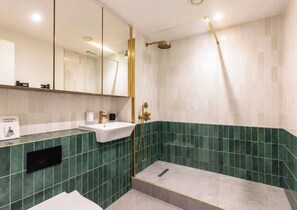 A modern bathroom with a glass shower enclosure, a white sink, and green-tiled walls. - Luxury City Centre Apartment with Canal View (West Midlands)