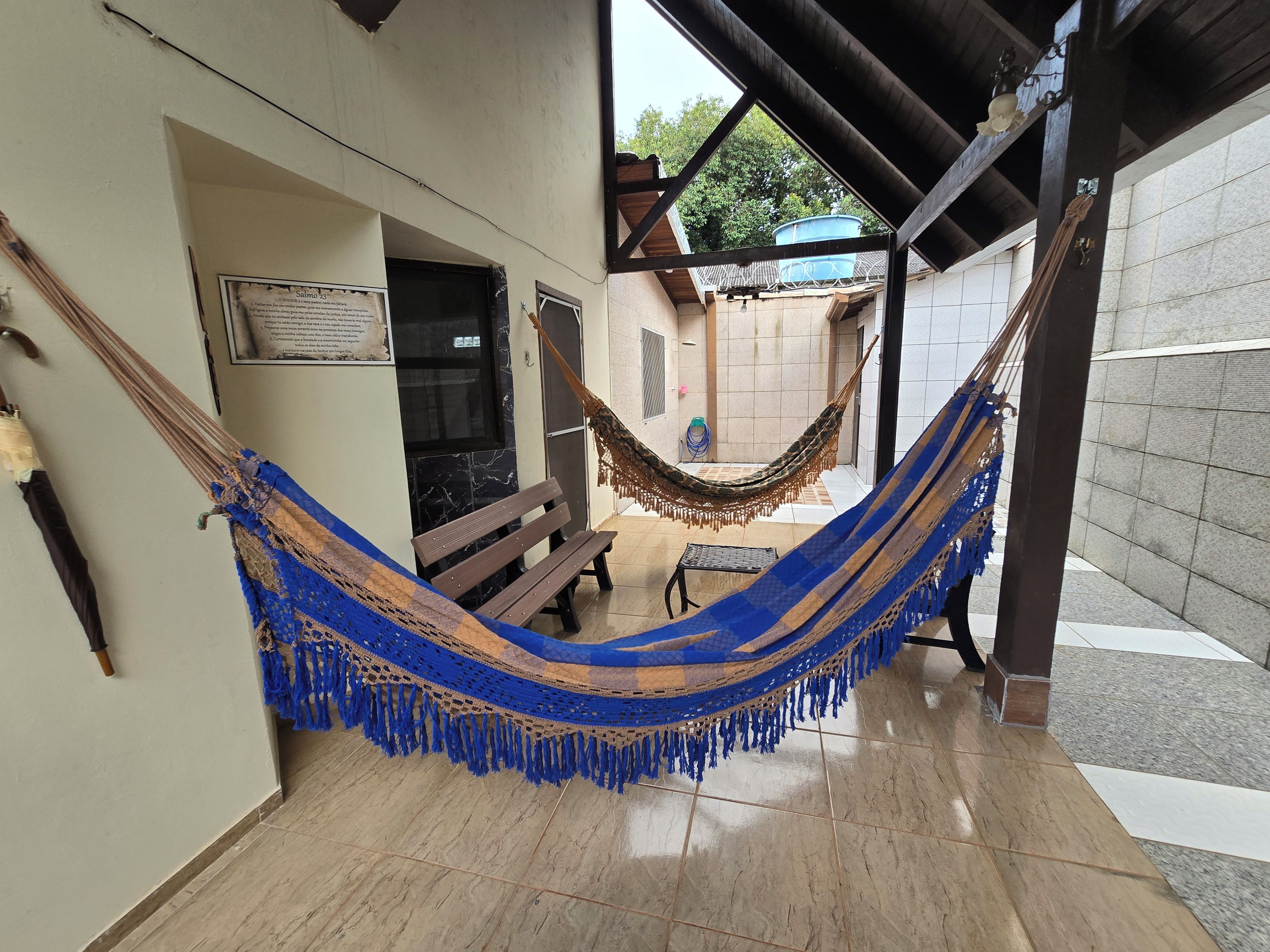 A hammock in a covered outdoor area with a bench and a tiled floor.