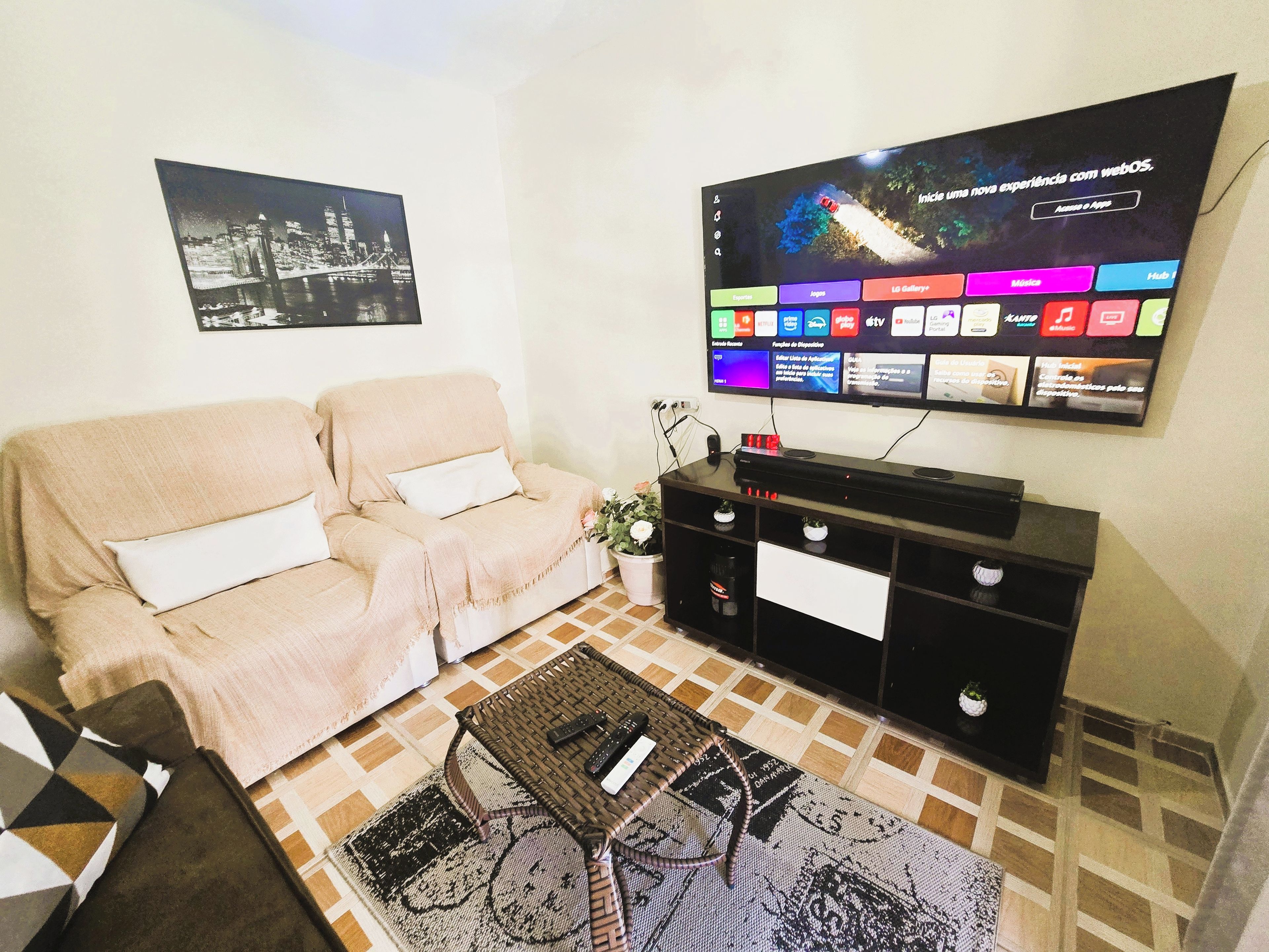 A living room with a beige sofa, a flat-screen TV mounted on the wall, a coffee table, and a patterned rug.