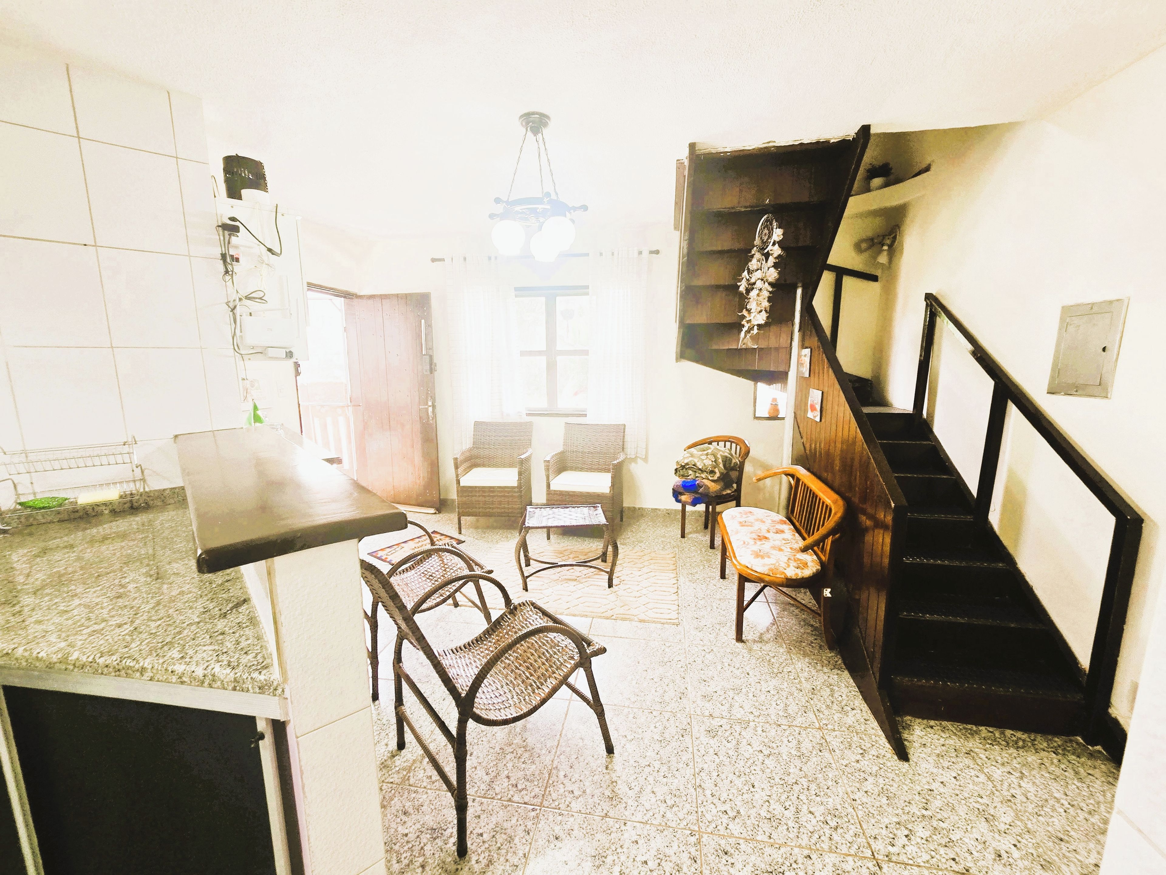A compact living space with a kitchen area, a dining table with chairs, a staircase, and a small seating area with a sofa and two chairs.