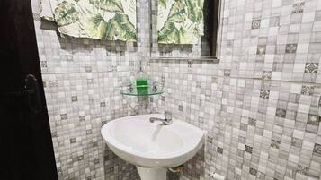Un baño con lavamanos pedestal blanco, un jabonero de vidrio, ducha de mano y un espejo.