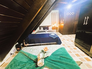 Un dormitorio en el ático con una cama, una manta verde y una toalla enrollada.