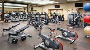 Un gimnàs amb diversos equips d'exercici, incloent cintes de córrer, el·líptiques i aparells de musculació.