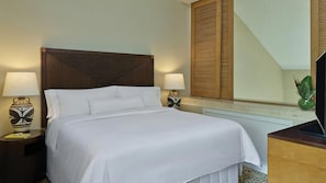 Un letto rifatto con lenzuola bianche, due lampade ai lati del letto, una testiera in legno, un grande specchio e una piccola pianta su un comodino.