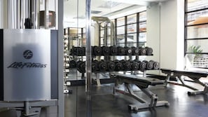 Ein Fitnessstudio mit Gewichtstrainingsgeräten, darunter Kurzhanteln und Bänke.