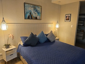 Een slaapkamer met een bed, nachtkastjes, een aan de muur hangend schilderij en een hanglamp.