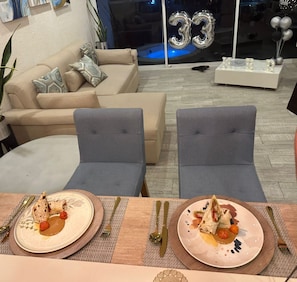 Een eethoek met twee grijze stoelen, een tafel met borden eten en een glazen raam met het nummer 33.