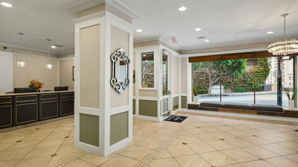 A reception area with a reception desk, a decorative mirror, a chandelier, and a view of the outside.