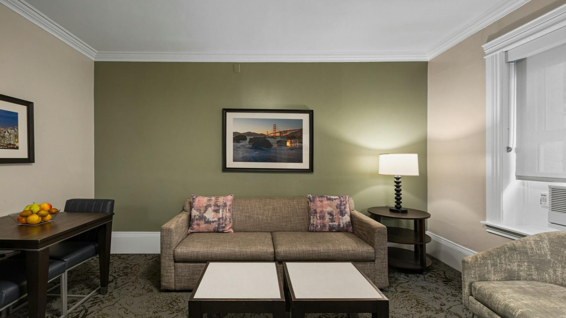 A living room with a sofa, two side tables, a lamp, a framed picture on the wall, and a small table with fruit.