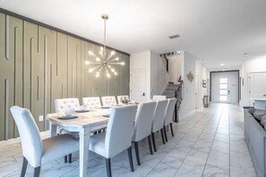 Un espace de salle à manger moderne, avec une table blanche dressée pour six personnes, un lustre contemporain et un escalier menant à un niveau supérieur.