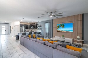A modern living room with a grey sectional sofa, a flat-screen TV, and a ceiling fan. - New Listing | Choose Your Own Adventure! 4 Themed Rooms, a Private Arcade and a Pool | Sleeps 25! (Kissimmee)