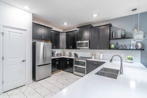 A modern kitchen with dark cabinets, stainless steel appliances, and a white countertop. - New Listing | Choose Your Own Adventure! 4 Themed Rooms, a Private Arcade and a Pool | Sleeps 25! (Kissimmee)