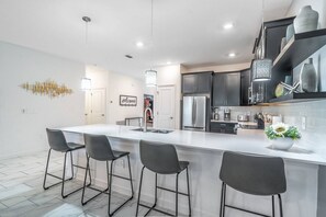 A modern kitchen with a large island, bar stools, and stainless steel appliances. - New Listing | Choose Your Own Adventure! 4 Themed Rooms, a Private Arcade and a Pool | Sleeps 25! (Kissimmee)