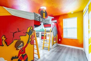 Une pièce décorée d’une fresque murale colorée sur le thème des super-héros, avec une échelle et une fenêtre munie de stores.