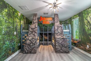 A room with a Jurassic Park themed entrance, a ceiling fan, and a window with blinds. - New Listing | Choose Your Own Adventure! 4 Themed Rooms, a Private Arcade and a Pool | Sleeps 25! (Kissimmee)