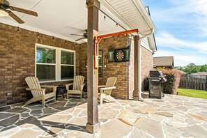 A patio area with a brick wall, stone flooring, and outdoor seating. - NEW! 4BR AU Club Home-Outdoor Fireplace & Game Room (Auburn)