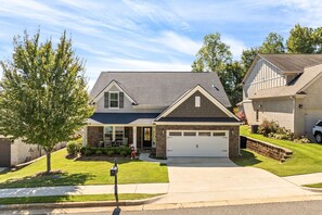 A two-story house with a garage, a front yard, and a tree. - NEW! 4BR AU Club Home-Outdoor Fireplace & Game Room (Auburn)