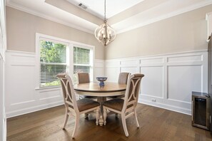 A dining area with a round table, four chairs, a chandelier, and a window with blinds. - NEW! 4BR AU Club Home-Outdoor Fireplace & Game Room (Auburn)