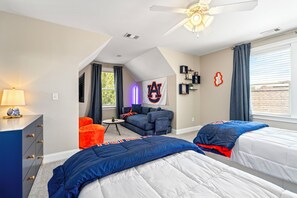 A bedroom with two beds, a desk, a chair, a ceiling fan, a window with curtains, and a flag on the wall. - NEW! 4BR AU Club Home-Outdoor Fireplace & Game Room (Auburn)