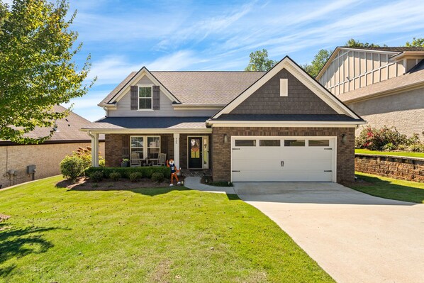 A two-story house with a garage, a covered porch, and a well-maintained lawn. - NEW! 4BR AU Club Home-Outdoor Fireplace & Game Room (Auburn)