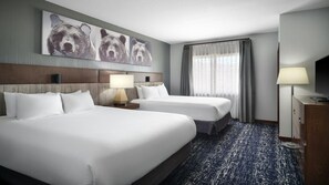 Een hotelkamer met twee bedden, een hoofdbord met een beer schilderij, een televisie, een lamp en een raam met gordijnen.