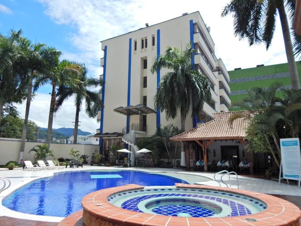 Un hotel con piscina, palmeras y un edificio con detalles azules.