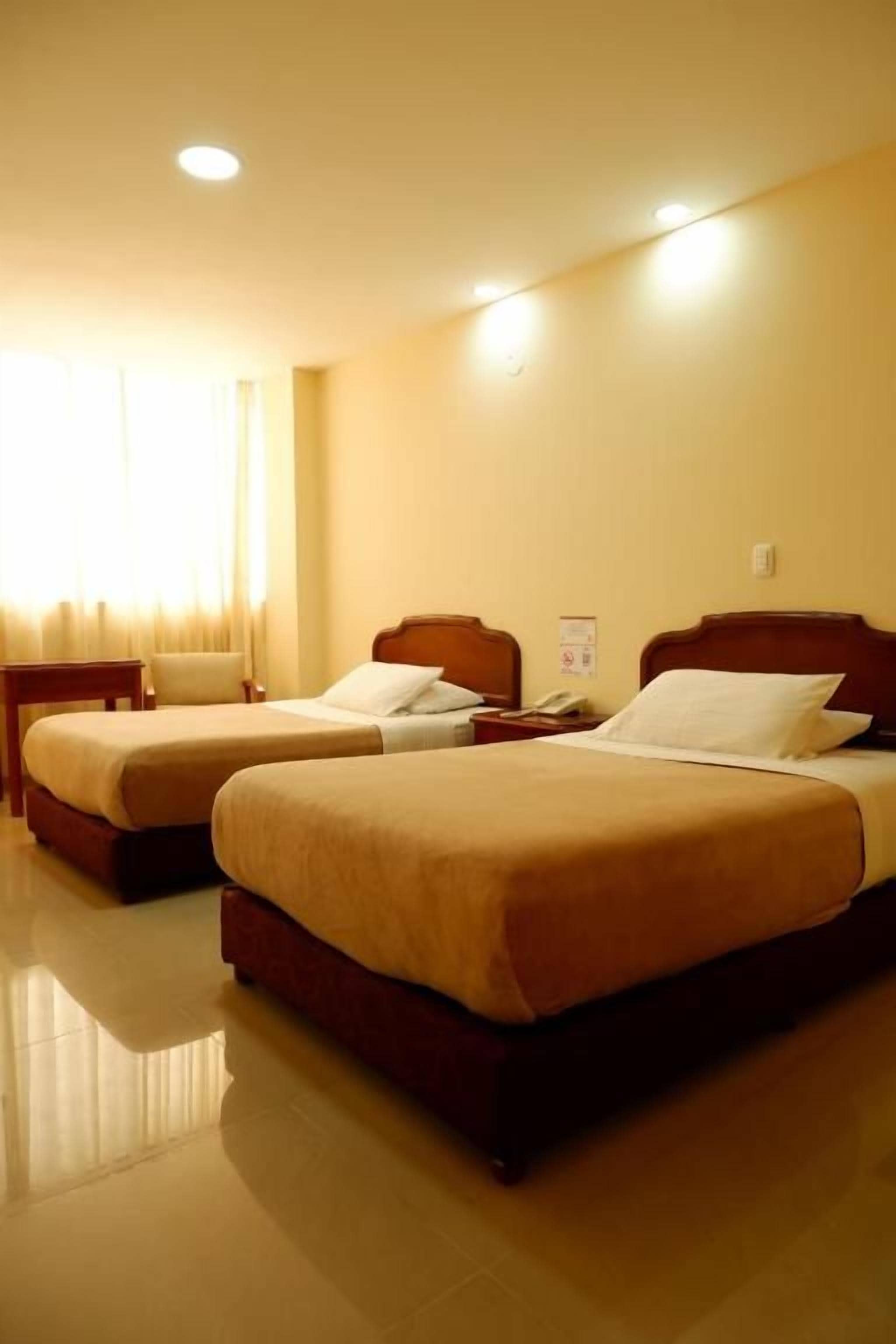 Habitación de hotel con dos camas, una mesita de noche y una ventana con cortinas.