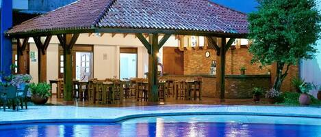 Zona de piscina con área de estar cubierta y un bar.