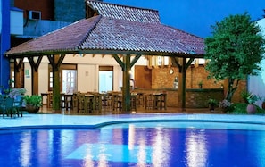 Zona de piscina con área de estar cubierta y un bar.