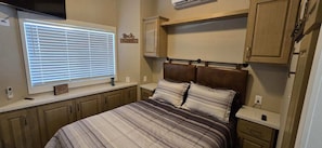A bedroom with a bed, a window with blinds, a cabinet, and a small table. - A15 Cozy 1-bedroom mobile home with AC in welcoming Casa Grande (Casa Grande)