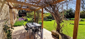 Eine Terrasse im Freien mit Tisch und Stühlen, umgeben von Grünpflanzen und einer Holz-Pergola.