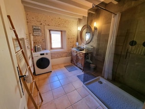 Ein kleines Badezimmer mit Waschmaschine, Waschbecken mit Spiegel und Duschbereich.