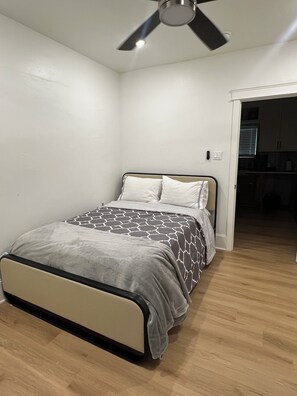 Une chambre à coucher avec un lit, un ventilateur de plafond et une porte donnant sur la cuisine.