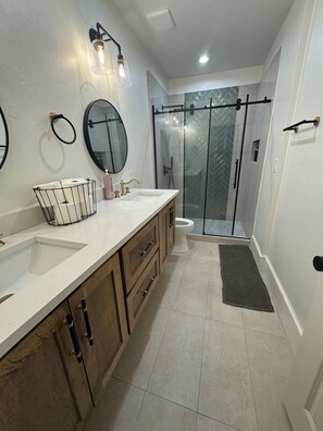 Une salle de bain moderne dotée d’un grand meuble-lavabo, de deux vasques, de toilettes et d’une douche à parois de verre.