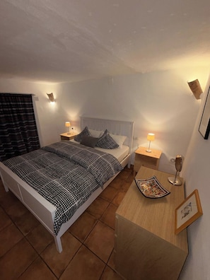Een slaapkamer met een bed, nachtkastjes, een lamp, een lijst met foto en een decoratieve kom.