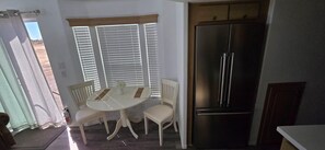 Une cuisine compacte équipée d’un réfrigérateur en acier inoxydable, d’une table à manger avec des chaises et d’une fenêtre avec des stores.