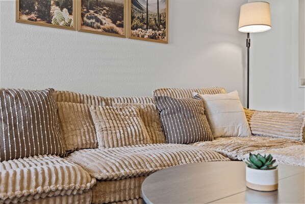 A modern living room with a sofa, multiple cushions, a round coffee table, a floor lamp, and a small potted plant. - Modern 3BR Mesa Home • Near Downtown, ASU (Mesa)