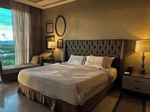 A hotel room with a large bed, a bedside table with a lamp, a nightstand, and a window with curtains. - PGA Open and Luxury Living in a 3 Bedroom Suite in sunny Mexico! (Nuevo Nayarit)